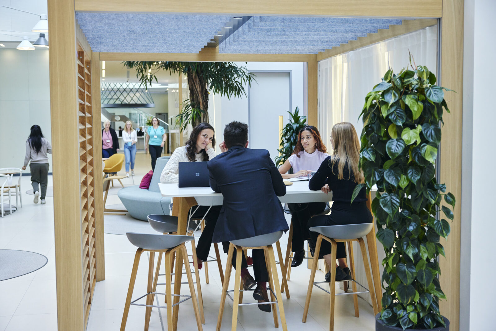 4 people sat to a high table in atrium area of office having a discussion