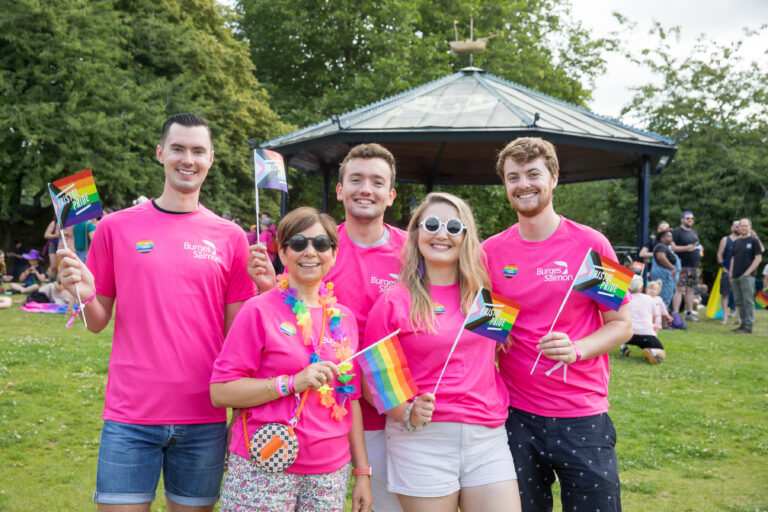 small group of people in burges salmon pride tshirts waving pride flags