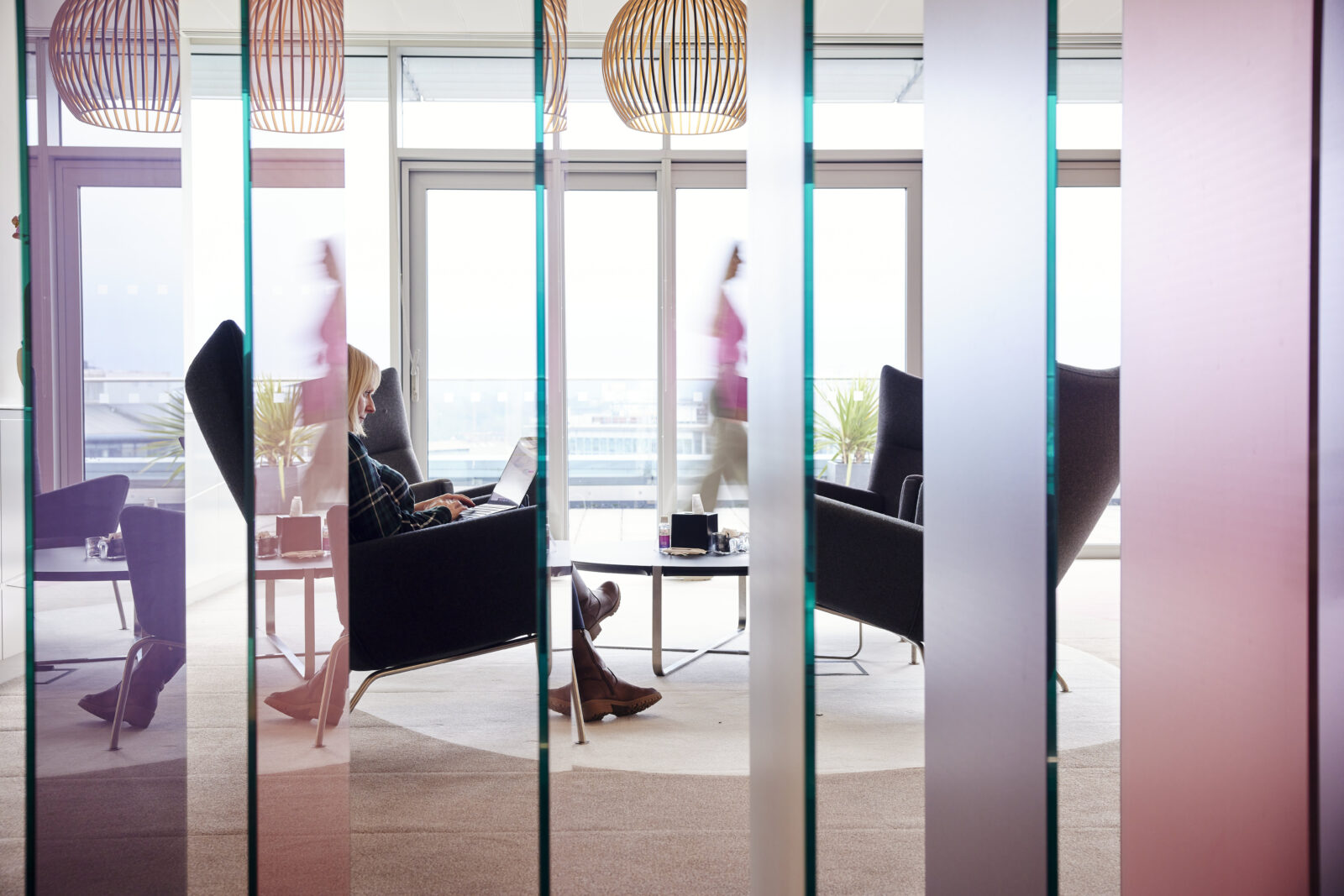 person in reception wait area on a laptop shown through glass panels