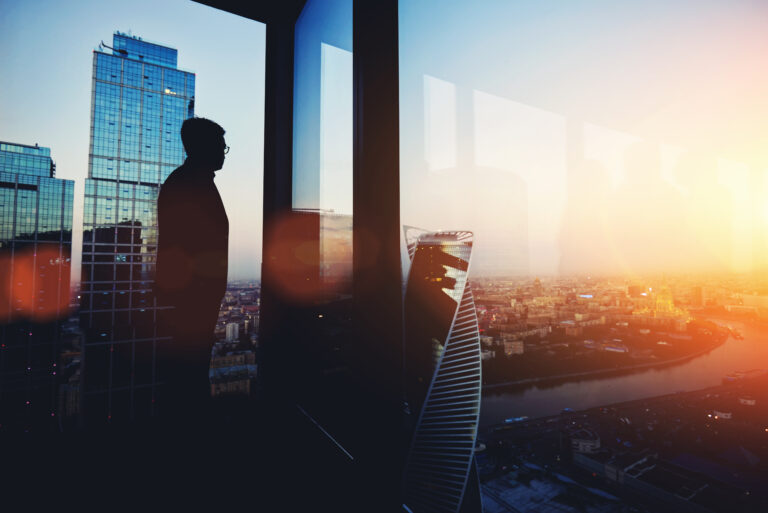 Silhouette of a Managing Director looking out the window of a tall commercial building at sunset