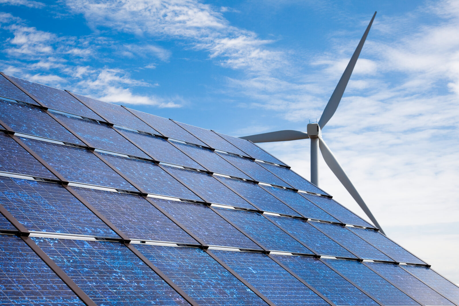 Inage of solar panels with a windfarm windmill in the background