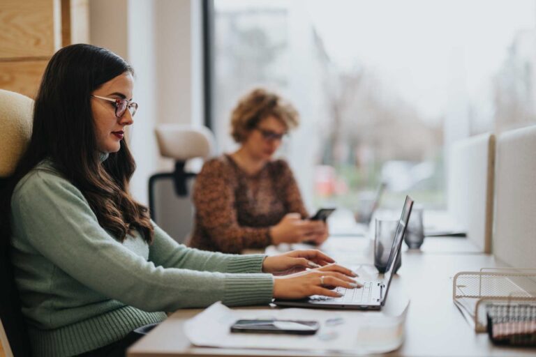 Two women at work with laptops and phone