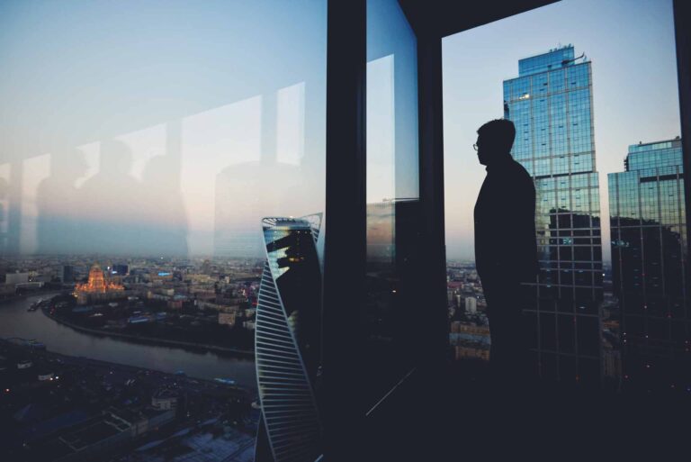Man looking out of a modern corporate skyscraper with a floor to ceiling window