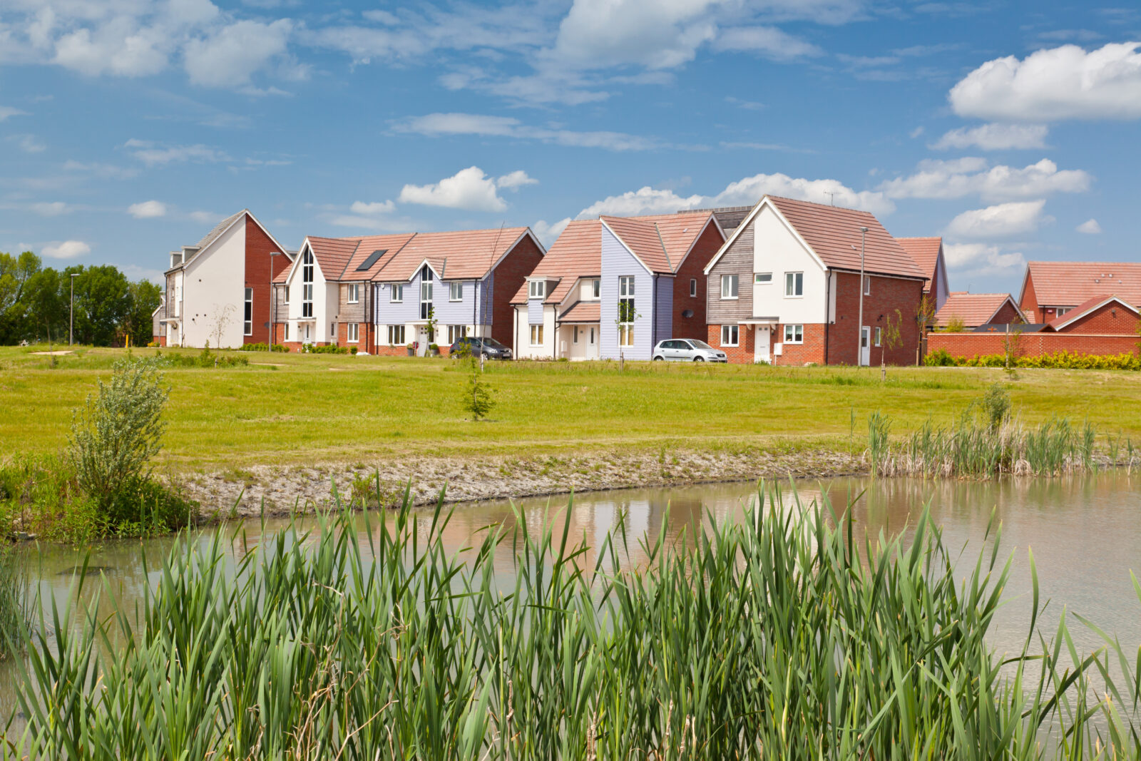 picture of a modern housing development with a field and pond in the foreground