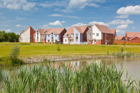 picture of a modern housing development with a field and pond in the foreground