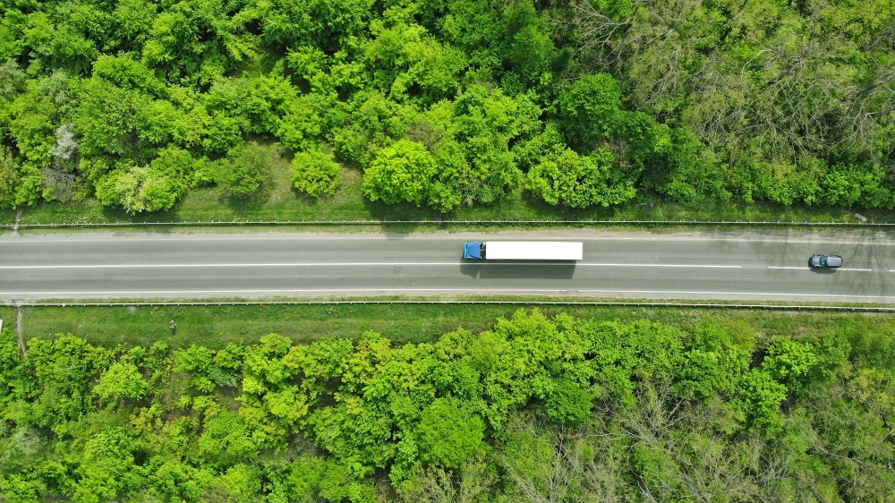 Aerial view of lorry driving along highway lined by trees