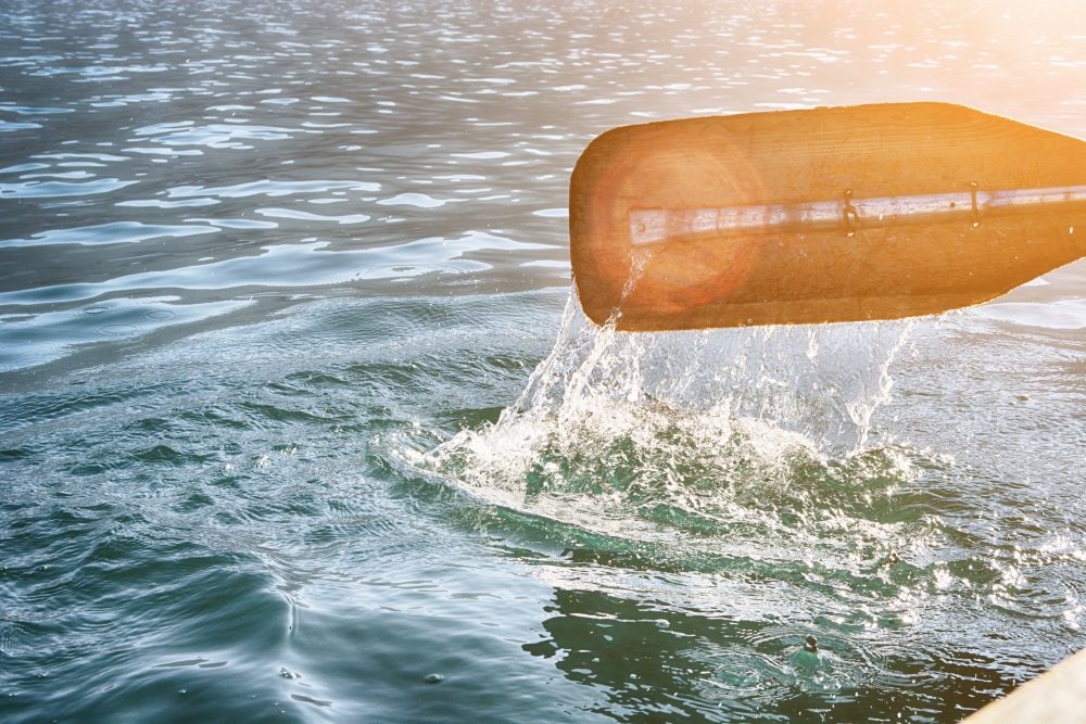 Oar of boat touching water and causing splash and ripples in the water