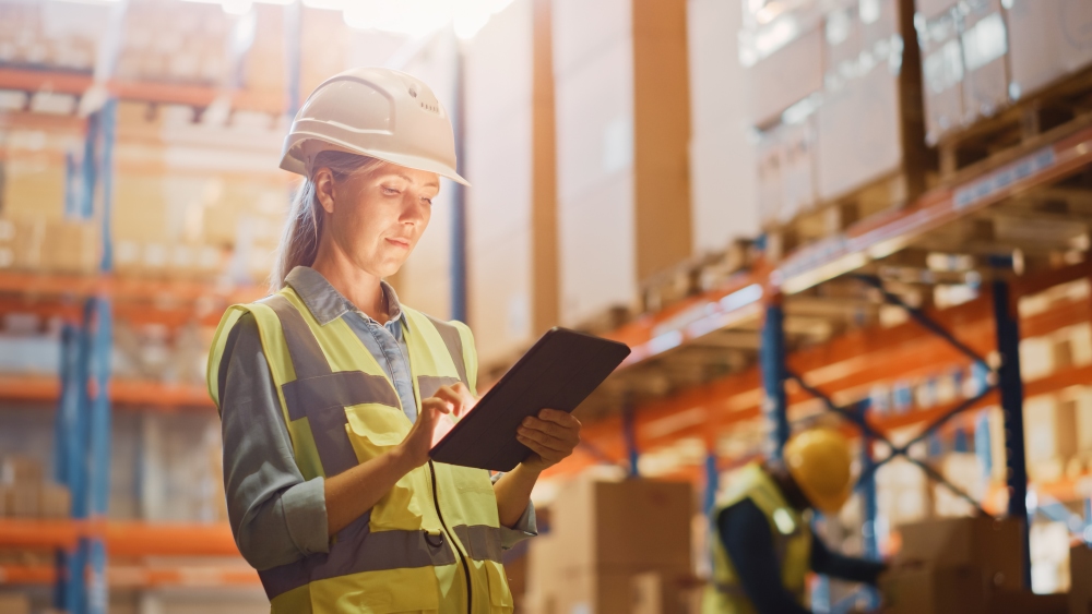 A female worker wearing hard hat in warehouse full of stocked shelves