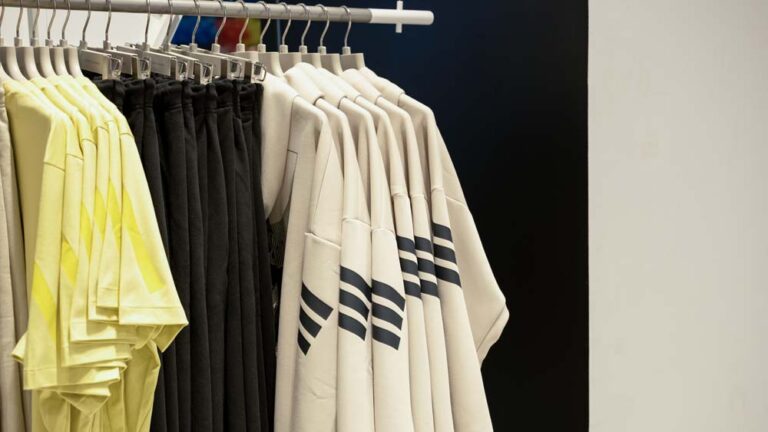 Adidas T-shirts and trousers in assorted colours neatly arranged on a clothing rack in a retail store with a minimal background