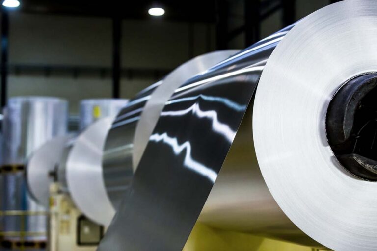 Large rolls of aluminium sheet being processed on industrial machinery in a factory