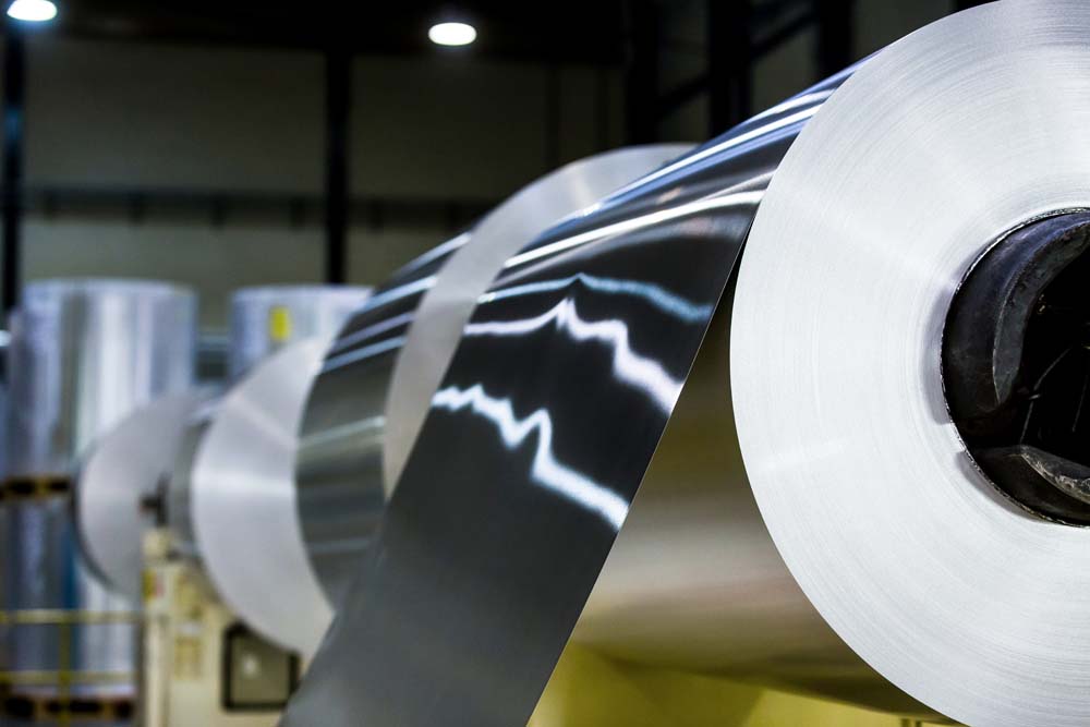 Large rolls of aluminium sheet being processed on industrial machinery in a factory