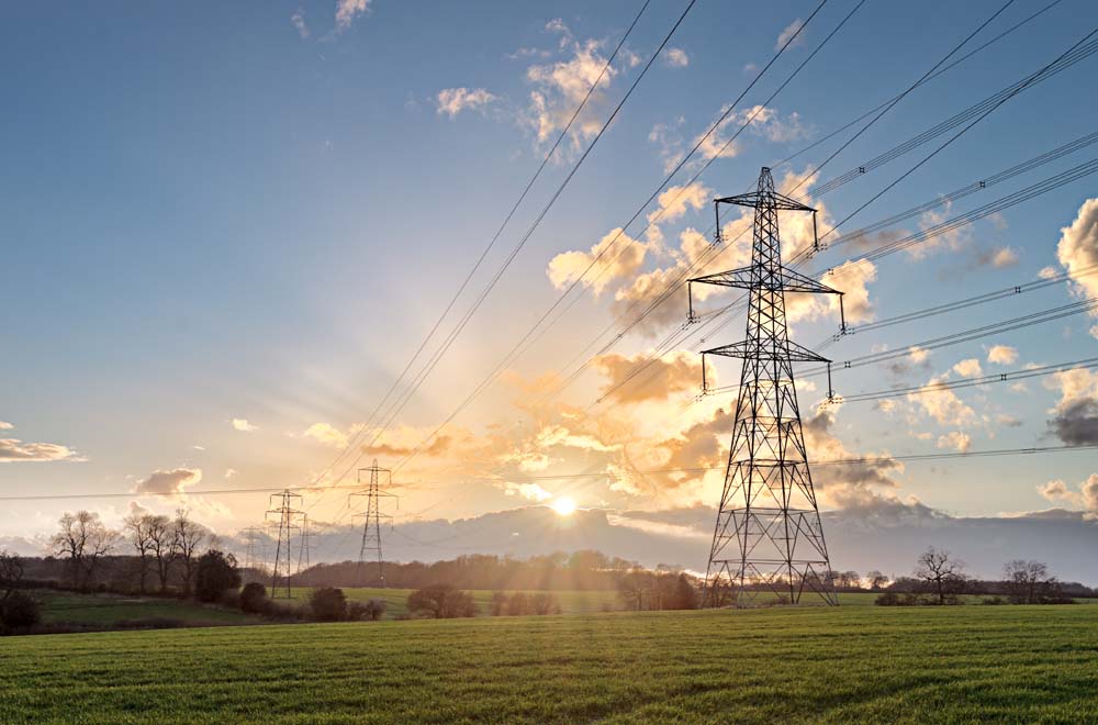 High voltage electricity pylon and overhead power lines across a rural landscape at sunset