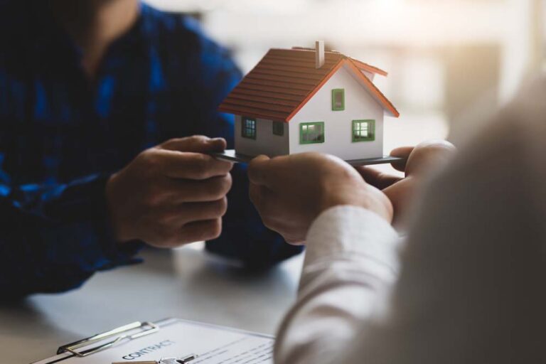 Model house passed between two people across a desk with paperwork