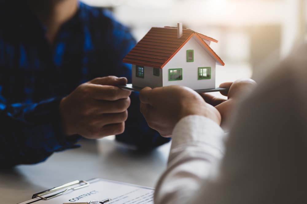 Model house passed between two people across a desk with paperwork