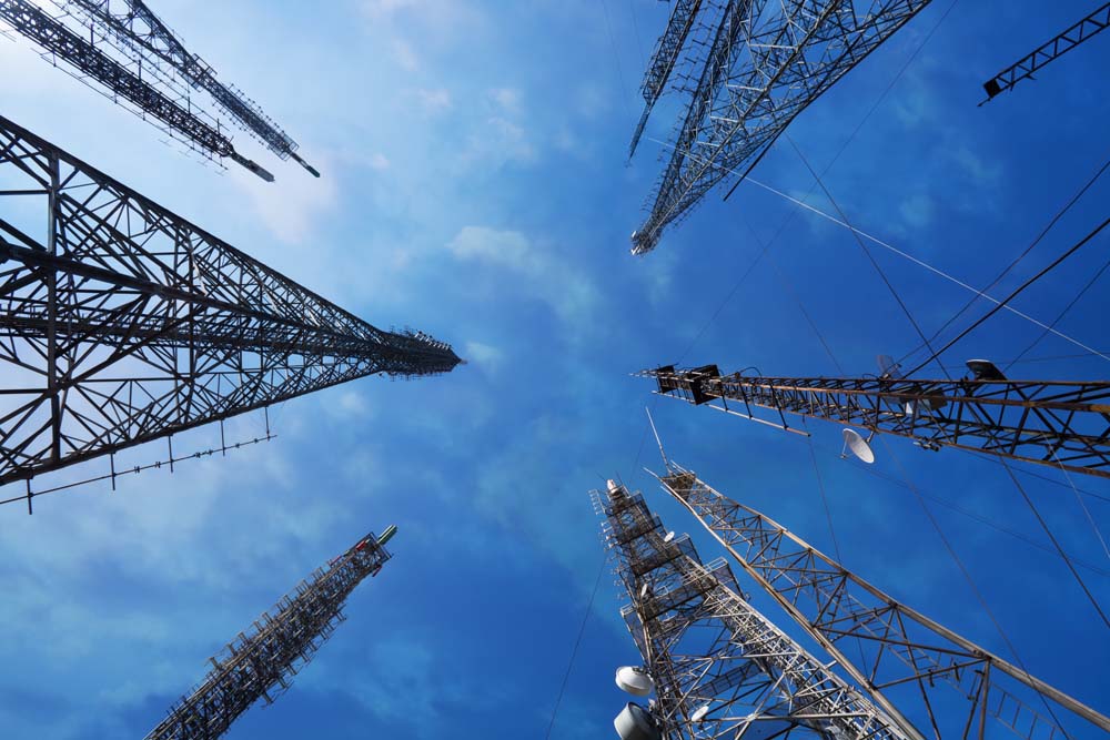 Telecommunications towers and pylons viewed from below against a blue sky