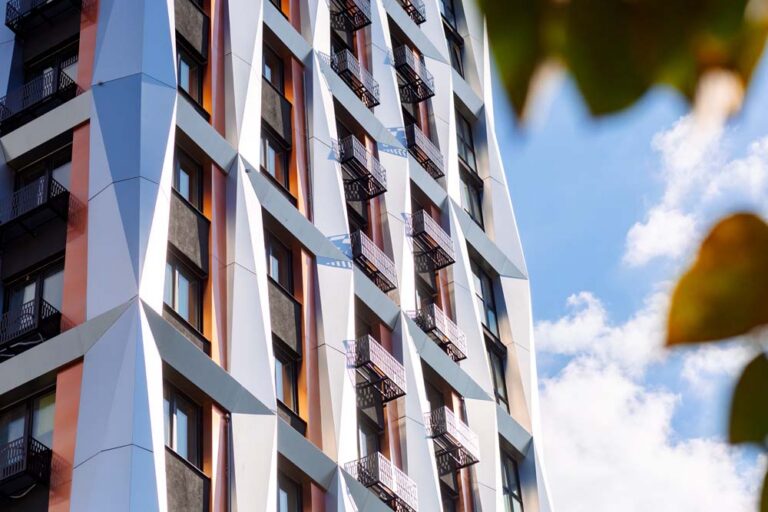 Modern apartment building with angular white cladding, balconies and large windows against a blue sky