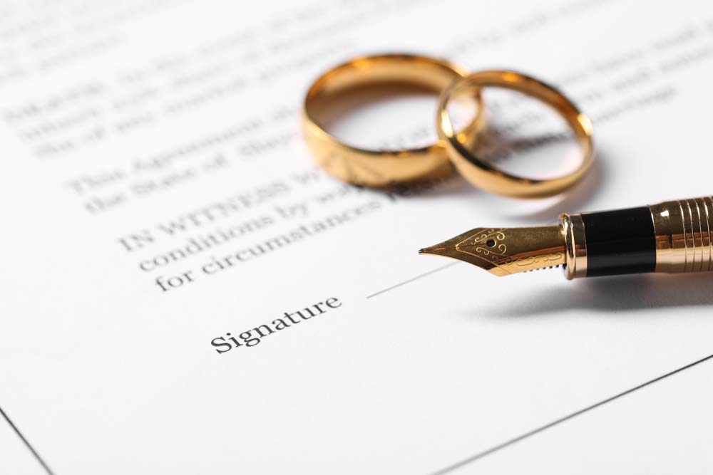 Gold wedding rings and a fountain pen on a pre-nuptial agreement signature page