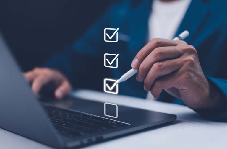 Person using a stylus next to a laptop with a digital checklist showing three completed tick boxes and one remaining item